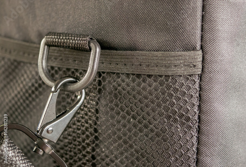 Photos Macro detail of a snap-hook (snap-link) fastened to the black bag with silver loop as a symbol of safety link between two objects