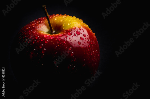 Red apple on black background covered in water drops