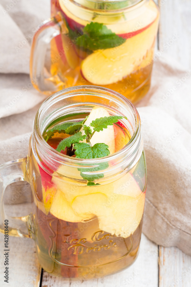 Cold tea with red apple, mint and cinnamon stick in a glass jar on a white background. Cold tea with red apple, mint and cinnamon stick in a glass jar on a white background.