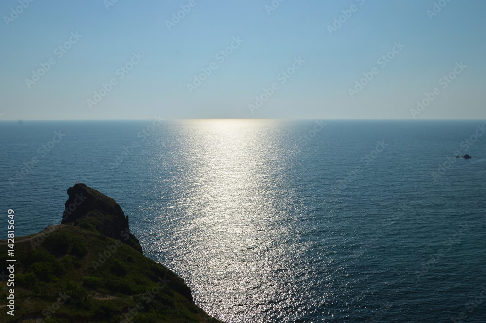 The green mountain goes to the sea. Visible horizon with a reflection of the sun at sea