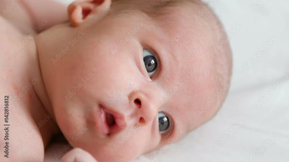 boy's face, the newborn child looking out the window at the light and lying on the white sheet and sneezes boy's face, the newborn child looking out the window at the light and lying on the white sheet and sneezes