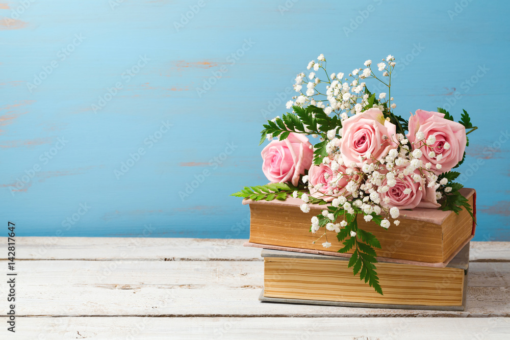 Fototapeta premium Rose flower bouquet on old books over wooden background with copy space
