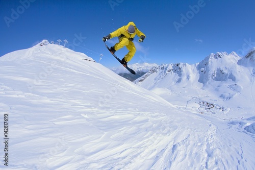 Snowboarder jumps in mountains, winter extreme sport.