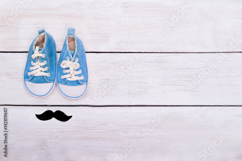 Child's blue sneakers and mustaches lie on a white wooden background. View from above