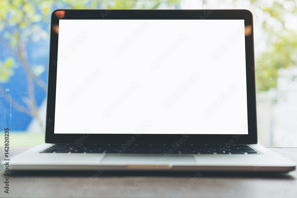 Mockup image of laptop with blank white screen on wooden table with blue sky and nature background through a mirror window