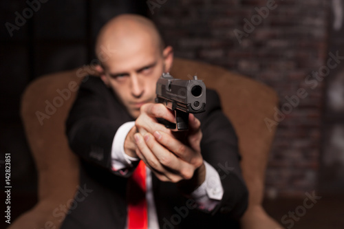 Bald killer in suit and red tie aims a pistol