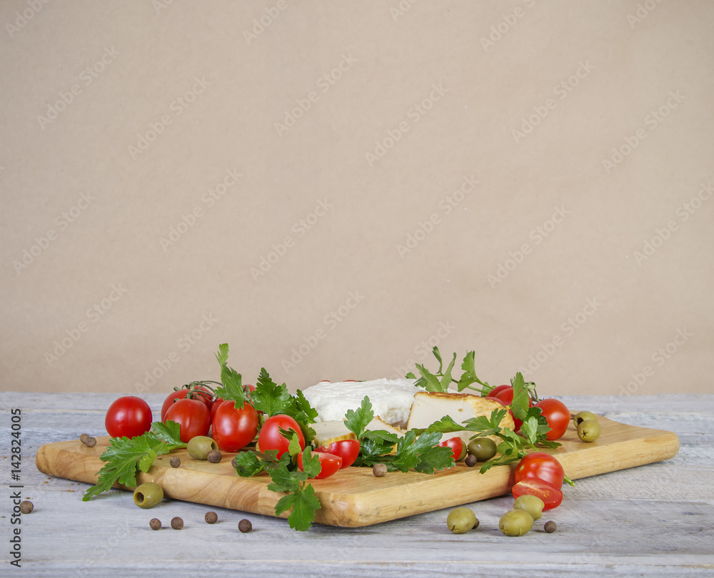 old paper background with homemade goat cheese, parsley, dill, onion, tomatoes and olives on wooden cutting board