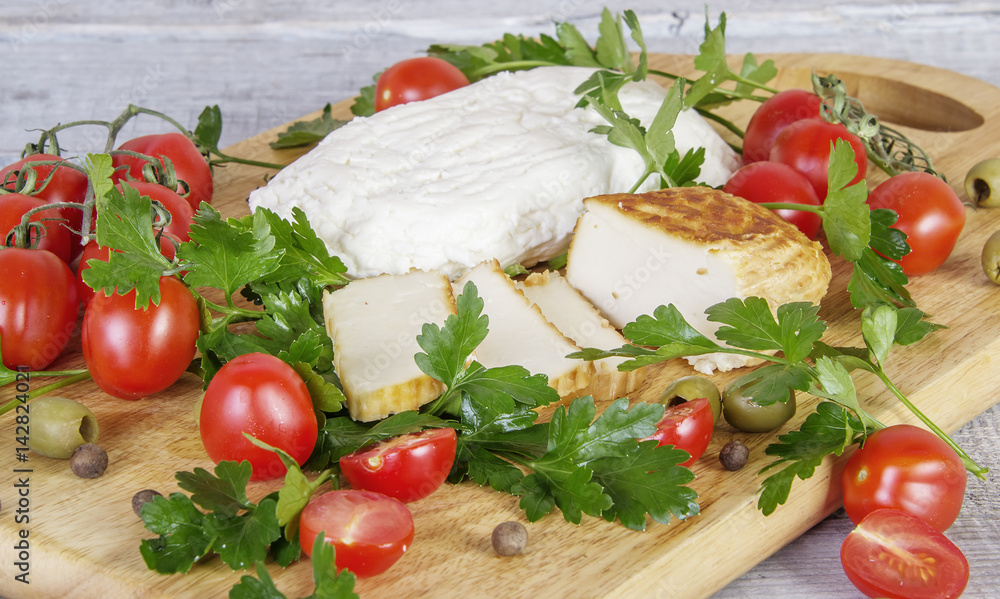 different kinds of homemade cheese, parsley, dill, onion, tomatoes and olives on wooden cutting board