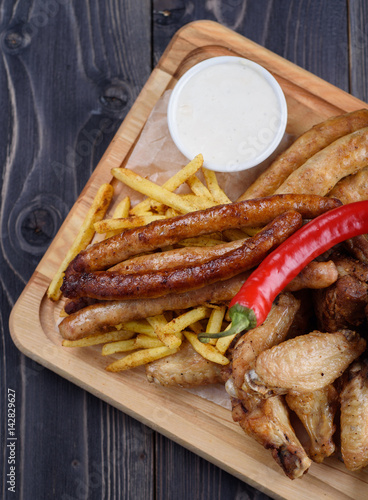 Grilled sausages and chicken with fries on a wooden board
