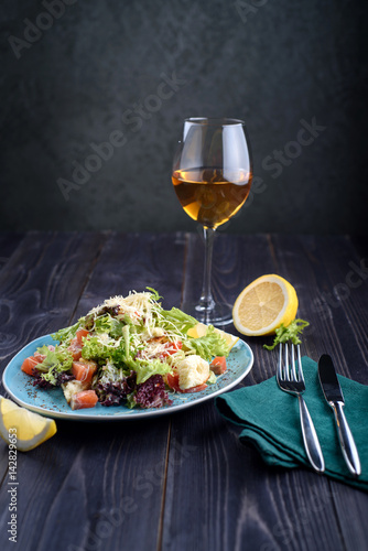Caesar salad with salmon in a blue plate on a wooden table and a glass of wine
