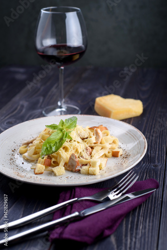 Pasta with meat and mushrooms on a white plate and a glass of wine