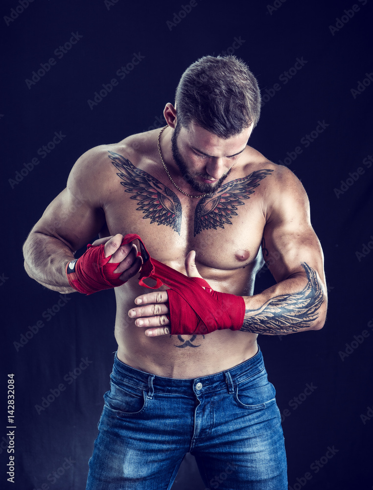 Muscular handsome topless boxer man preparing red gloves, looking down, in studio shot against black background