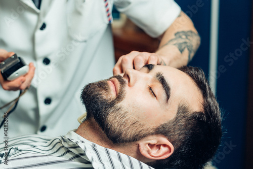 portrait of handsome man with beard in barbershop. barber working with electric razor