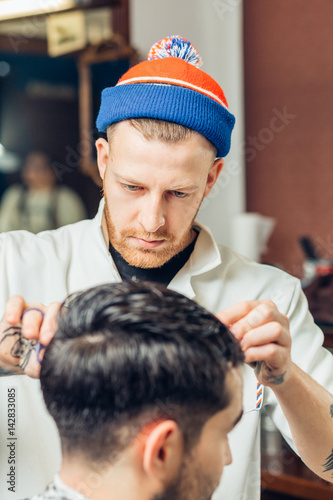 Joyful conversation. Cheerful skillful barber making a haircut with scissors to a young bearded man