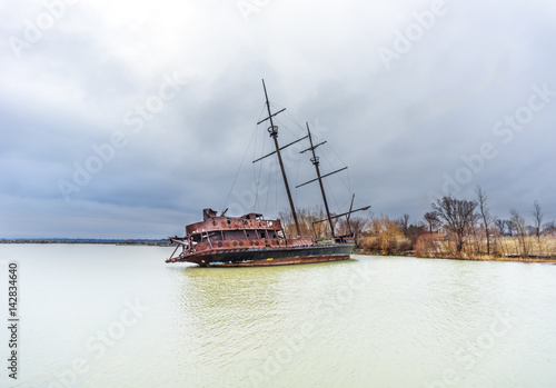 Rusty shipwreck marooned near shore on lake under a stormy blue sky