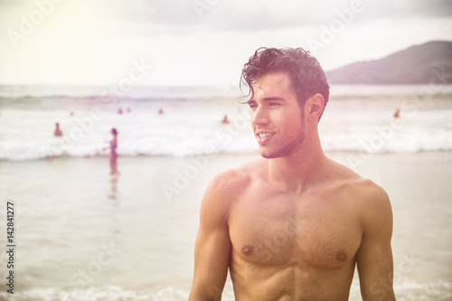 Heavily filtered shot of a handsome young man standing on a beach in Phuket Island, Thailand, shirtless wearing boxer shorts, showing muscular fit body
