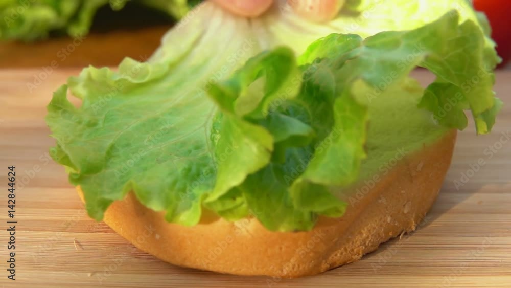 Chef puts green lettuce leaf on a bun Chef puts green lettuce leaf on a bun