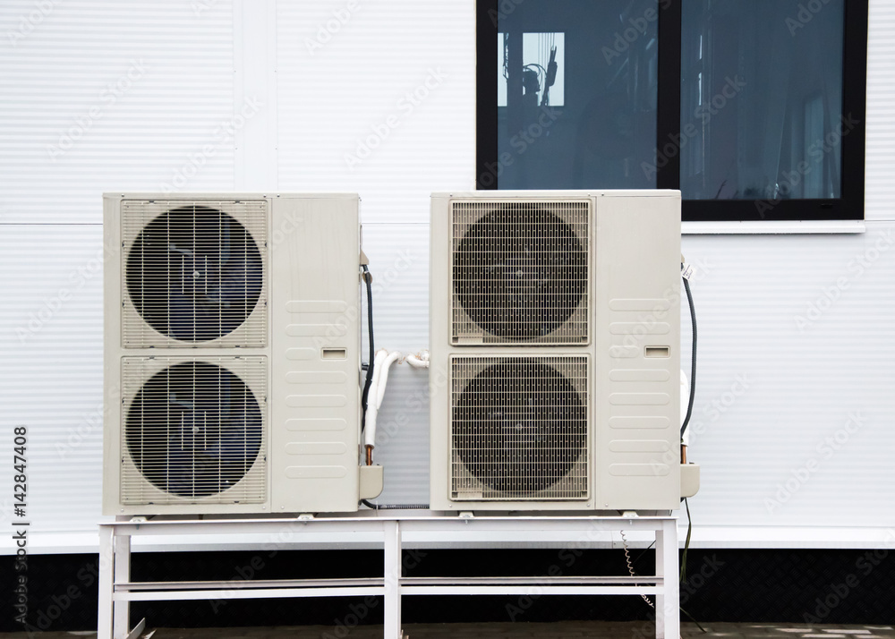Two outdoor units of air conditioners standing on the ground in front ...