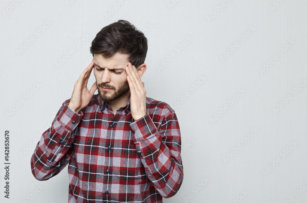 Portrait of attractive young man with beard holding her head suffering from pain. Migraine and headache. Overworked, stressed and have business problems. Portrait of attractive young man with beard holding her head suffering from pain. Migraine and headache. Overworked, stressed and have business problems.