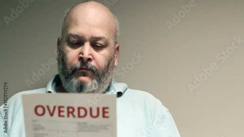 Depressed man looking at overdue bill, then looks at screen