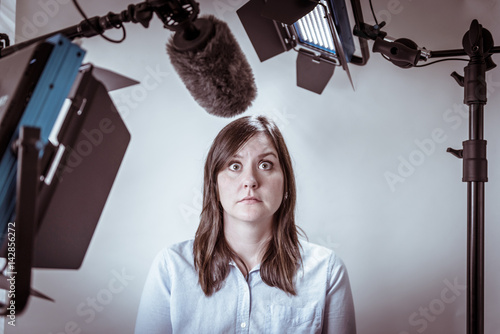 Scared and nervous business woman under video lights and microphone about to be interviewed on camera.