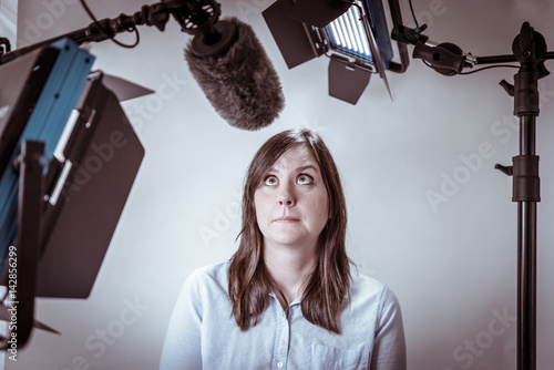 Scared and nervous business woman under video lights and microphone about to be interviewed on camera.