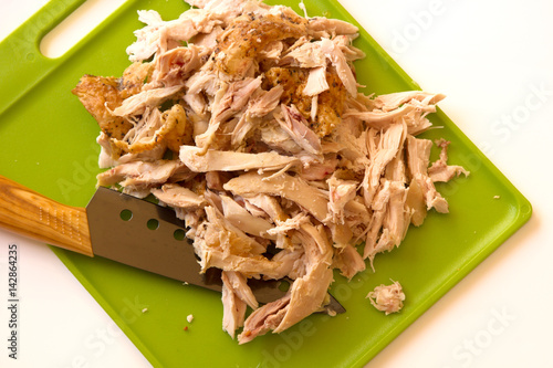 Obraz na plátně Shredded rotisserie chicken on a green cutting board and carving knife isolated