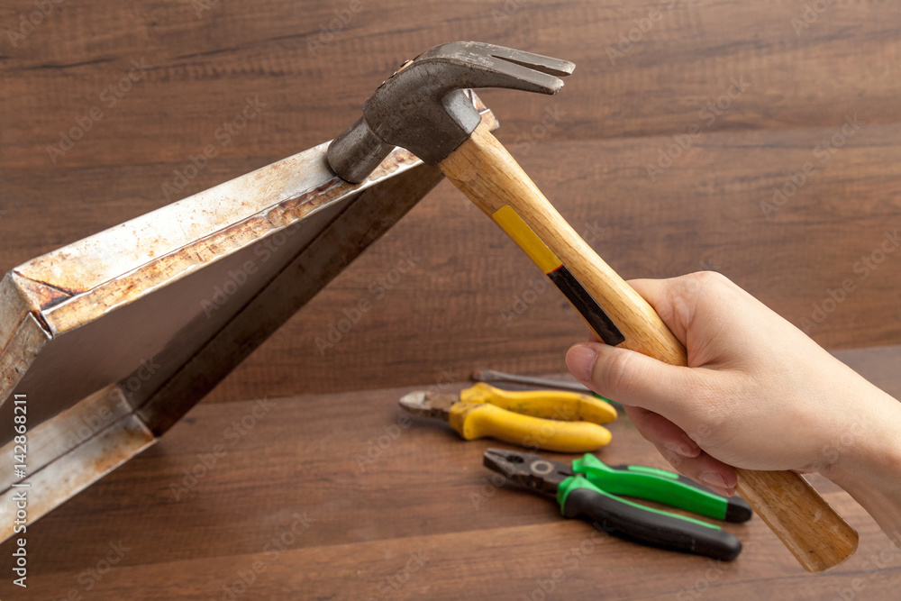 Man handle hammer to hit or fix stainless tray on wooden background.