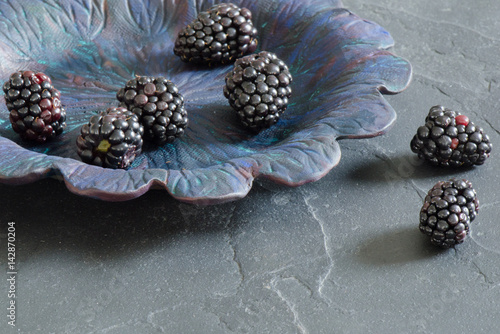 Fototapeta Naklejka Na Ścianę i Meble -  Dark, moody image of black berries on a pottery plate on black slate