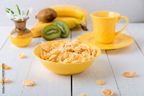 Healthy breakfast with cereal flakes and fruit near vase with flowers on white background. Yellow tone