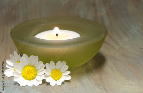 A Candle in a glass holder with white daisy flowers