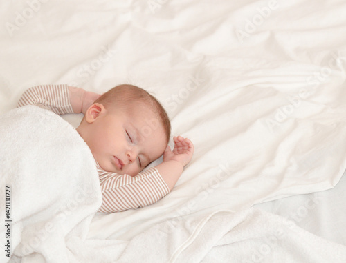 Peaceful baby lying on a bed while sleeping in a bright room