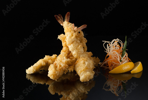 shrimp in tempura with lemon slices and salad on a black background with reflection photo