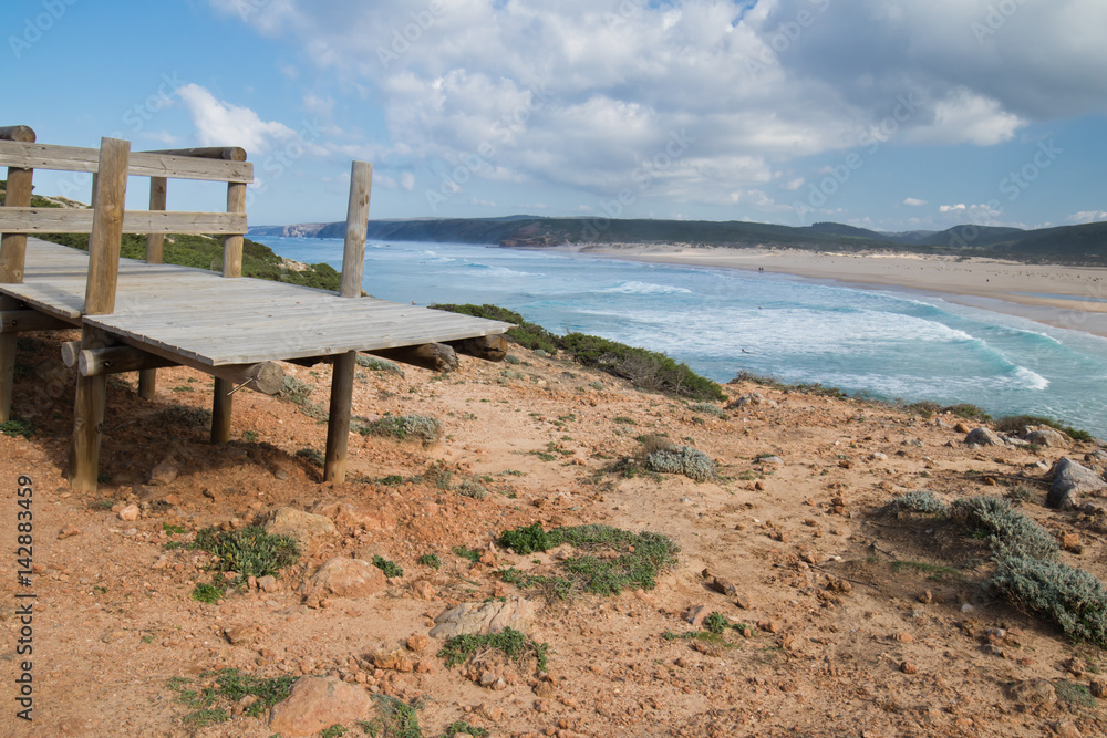 broken wooden pathway with stunning overhanging view on beautiful atlantic coast with beach of bordeira from cliff ledge, popular surf destination in algarve, portugal