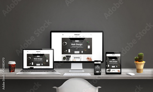 Web design studio with responsive web site promotion. Computer display, laptop, tablet and smart phone mockup on office desk. Plant and coffee beside. photo
