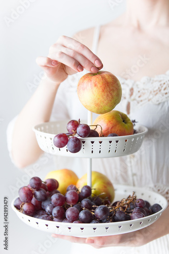 photo of young woman holding stand with fruits on the wonderful white background