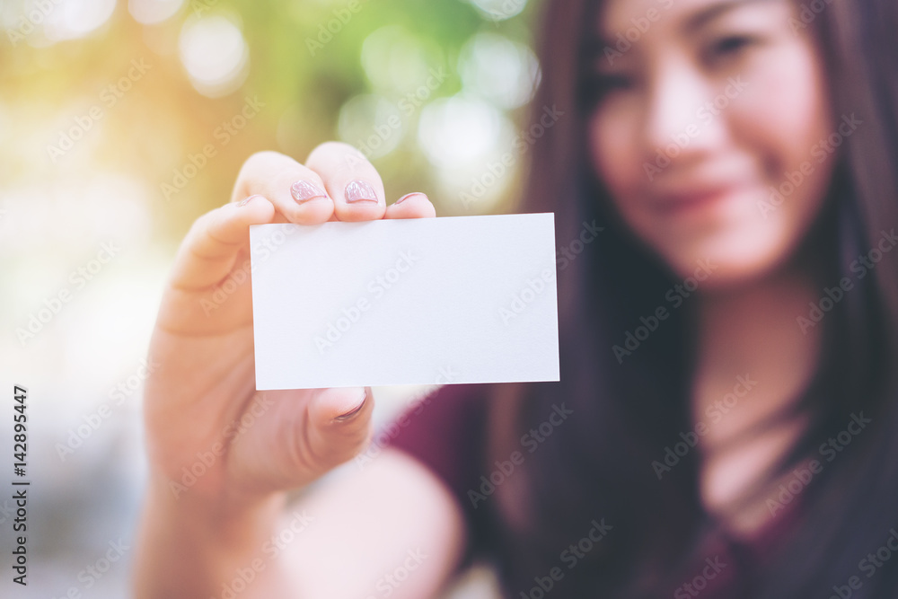 A beautiful woman holding and showing empty business card with smiley face in nature background A beautiful woman holding and showing empty business card with smiley face in nature background