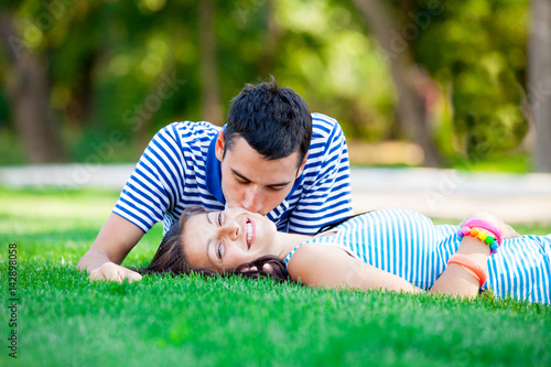 photo of cute couple kissing and lying on the grass in the field