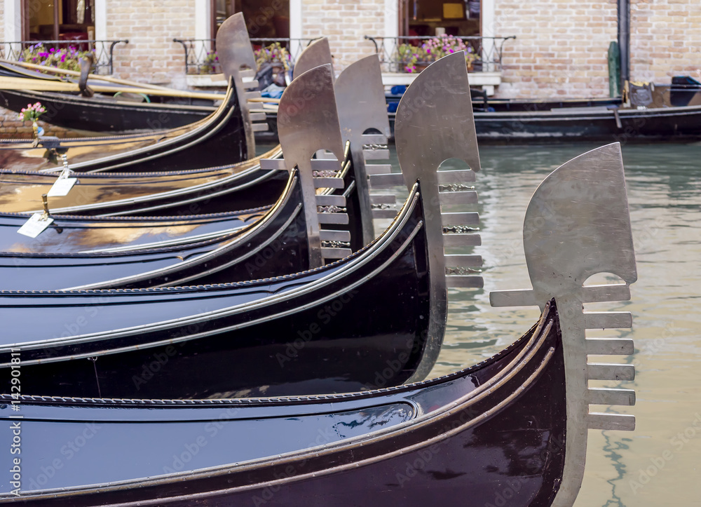 Beautiful row of metal bows of traditional Venetian gondolas anchored in a canal in the San Marco district, Venice, Italy