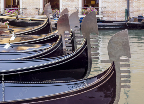 Beautiful row of metal bows of traditional Venetian gondolas anchored in a canal in the San Marco district, Venice, Italy #142901811