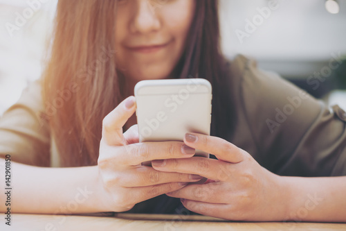 A beautiful Asian girl with smiley face using smart phone in modern cafe