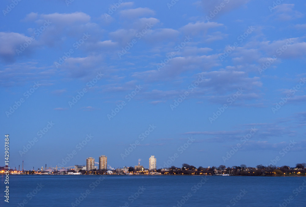 Residential and industrial cityscape and vast cloudscape seen at dusk from across a deep blue lake