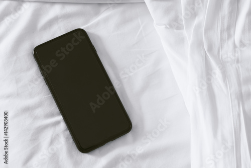 Top view of black smart phone on the bed.