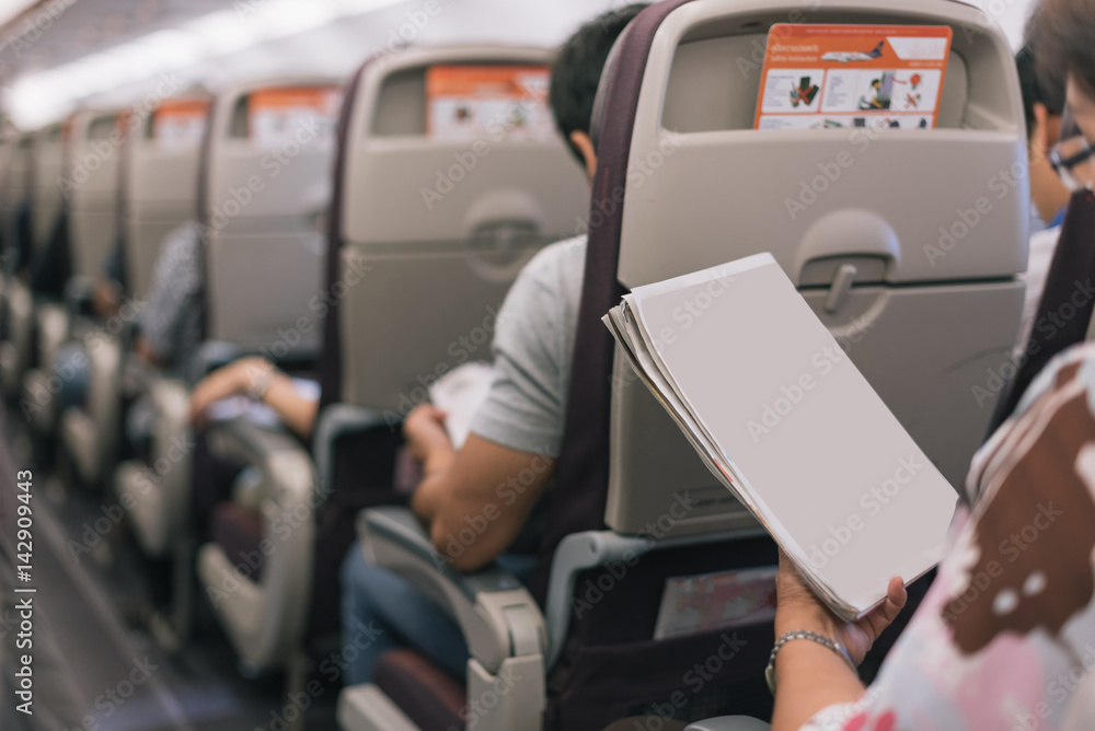 Naklejka premium Passenger reading a magazine at a her seat on the airplane in selective focus.