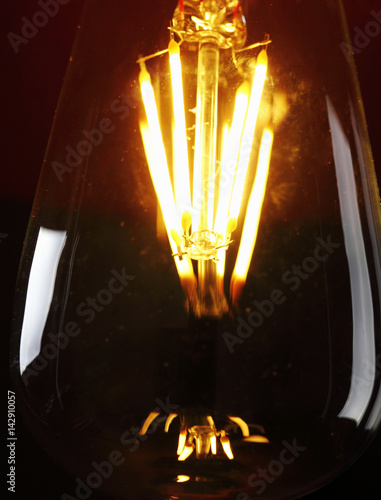 Red light bulb close-up glowing on a red elegant background - beautiful large filament photo