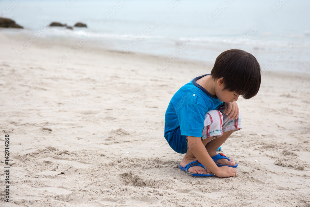 4 years old Asian boy sand writing lonely on beach with sea background and copy space 4 years old Asian boy sand writing lonely on beach with sea background and copy space