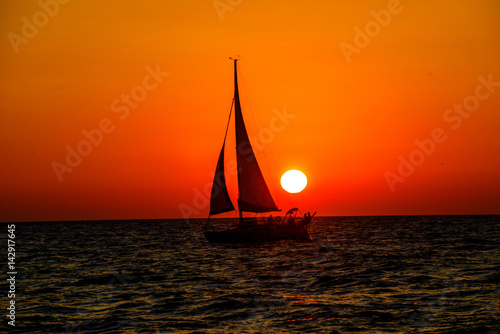 full sail sailboat past yellow sunset in the ocean with orange skies sailboat is a silhouette