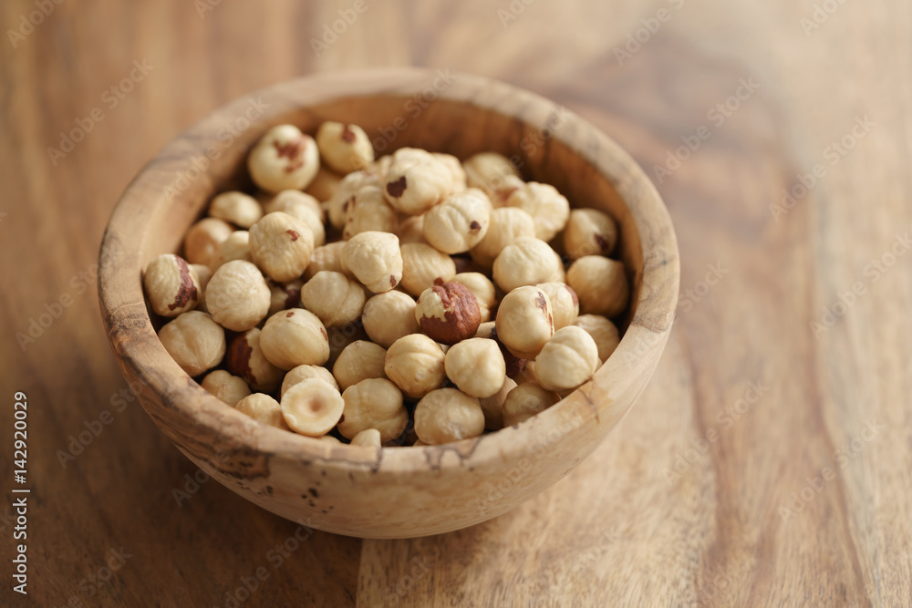 roasted hazelnuts in wood bowl on wooden table, copy space on the right side roasted hazelnuts in wood bowl on wooden table, copy space on the right side