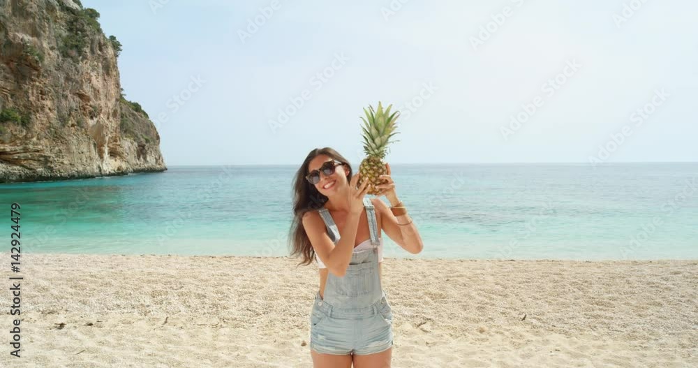 Happy woman balancing pineapple on head posing for camera being silly and playful on tropical beach summer vacation holiday Happy woman balancing pineapple on head posing for camera being silly and playful on tropical beach summer vacation holiday