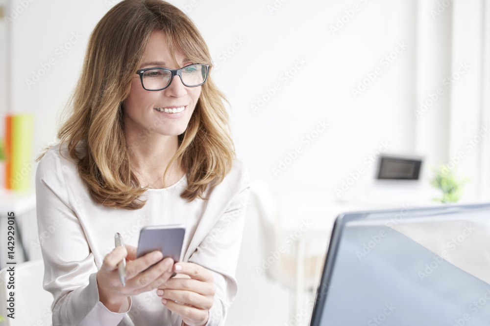 Executive professional woman. Shot of an confident general manager businesswoman using her mobile phone and text messaging while sitting in front of laptop. Executive professional woman. Shot of an confident general manager businesswoman using her mobile phone and text messaging while sitting in front of laptop.